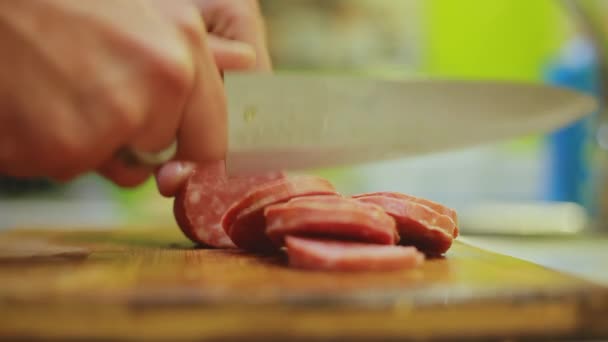 Чоловік розрізає жирну ковбасу ножем на дерев'яній дошці. Крупним планом — стокове відео