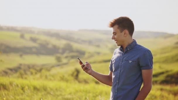 El joven usa un teléfono móvil al aire libre. Tiene en sus manos su smartphone. Primer plano . — Vídeo de stock