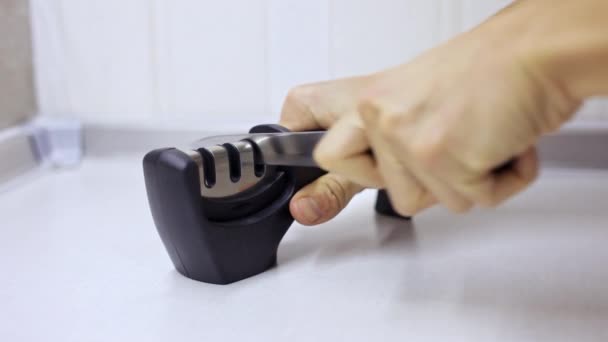 Manual sharpening of a knife in a special sharpener in a kitchen, man hands in close-up — Stock Video