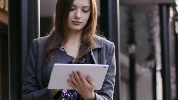 Крупным планом портрет красивой молодой предпринимательницы, которая пользуется планшетом на улице на закате возле бизнес-отеля — стоковое видео