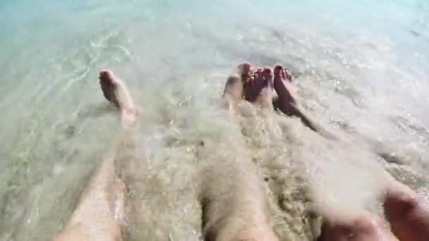 人们的脚被海浪冲走, 埋在沙子里。一男一女脚躺在沙滩上的特写镜头 — 图库视频影像