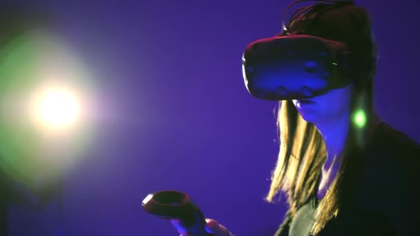 Mujer jugar juego de realidad virtual 3D. Dispara con los controladores en un juego de disparos VR. Chica con auriculares VR, destello de luz en el fondo — Vídeo de stock