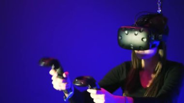 Kadın oyun 3d sanal gerçeklik oyunu. Bir tetikçi denetleyicileriyle Vr oyun vuruyor. Mavi arka plan üzerinde VR kulaklık giyen kız