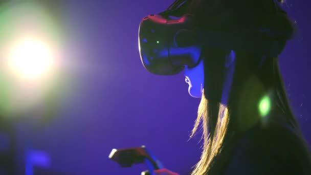 Emotional woman play 3D virtual reality game. Shoots with controllers, looking around. Girl wearing VR headset, light flare on backround — Stock Video