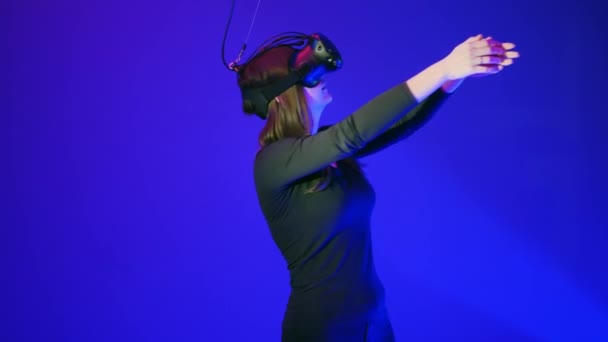 Ung kvinna i Vr-headset ha kul och spela interaktiva spel. Virtual reality hjälm på blå bakgrund, gestikulerande — Stockvideo