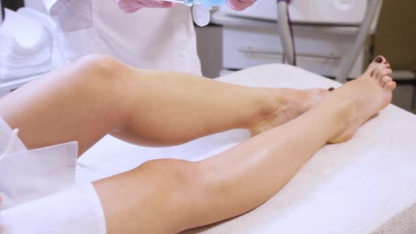 Προετοιμασία των ποδιών για μια αποτρίχωσης με λέιζερ, η γυναίκα βάζει κρέμα. — Αρχείο Βίντεο