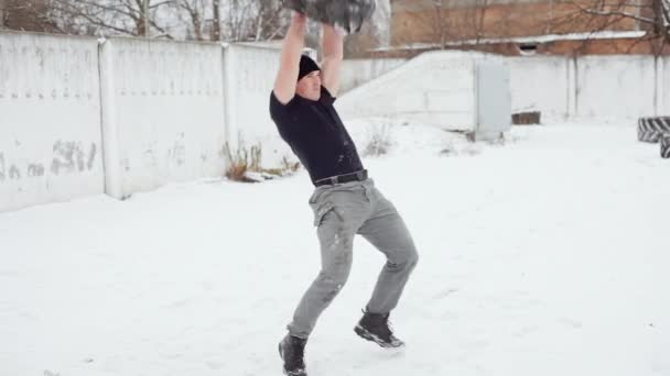 М'язистий чоловік кидає гумову шину над собою, роблячи кросфітові вправи взимку — стокове відео