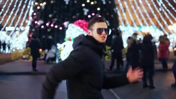 El hombre de estilo en los cristales el baile divertido en la velada al nuevo año sobre el árbol de Navidad de la ciudad — Vídeos de Stock