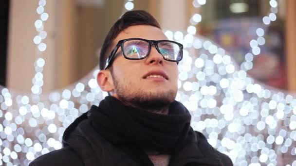 Stílusos szakállas férfi, a karácsonyi fények és a város új év Tree ünnepeljük tükröződik a szemüveg — Stock videók