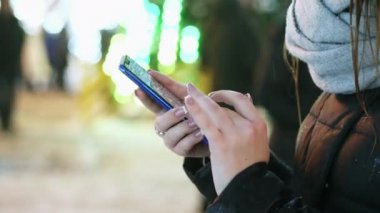Bir kadının el closeup karlı akşamları, ışıklar ve süslemeleri Noel ve yeni yıl için yakın hareket eden app kullanır