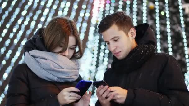 Beau couple utilise l'application mobile dans la soirée enneigée, Noël et Nouvel An — Video
