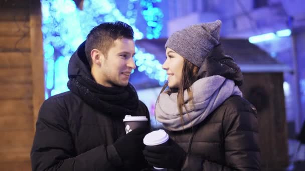 Gelukkige paar koffie drinken op de kerstmarkt onder de sneeuwval. Prettige kerstdagen en gelukkig Nieuwjaar — Stockvideo