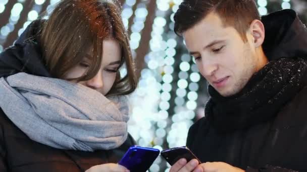 Κοντινό πλάνο ζευγάρι όμορφη κινητό app χρησιμοποιεί το χιονισμένο βράδυ Χριστουγέννων και Πρωτοχρονιάς — Αρχείο Βίντεο