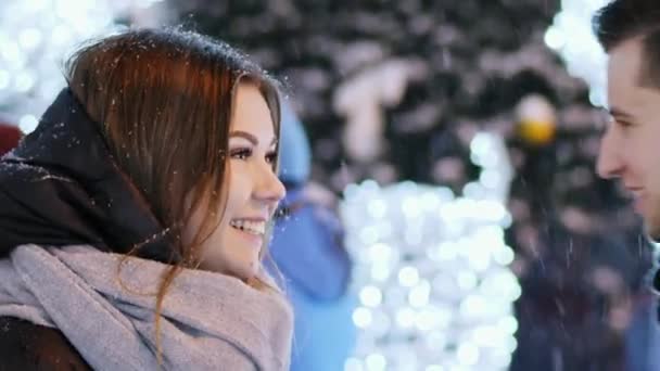 Primo piano uomo dà un regalo a una donna per strada decorata con luci e ghirlande, Capodanno e Natale — Video Stock