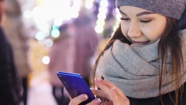 Närbild av ung kvinna använder mobilappen på snöiga kvällen, jul och nyår — Stockvideo