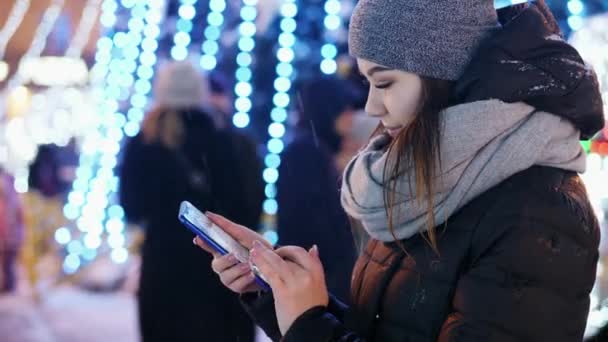 Primer plano de la hermosa mujer utiliza la aplicación móvil en la noche nevada, Navidad y Año Nuevo — Vídeo de stock