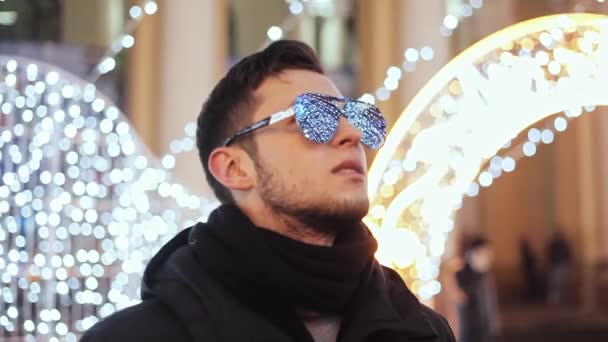 Şık adama kutlama yeni yıl, Noel ağacı, çelenk ve yansıtılmış güneş gözlüğü yansıyan ışıklar şehir — Stok video