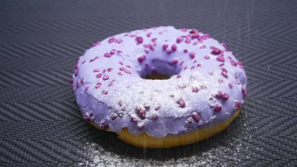 Посыпать сахарной пудрой фиолетовый пончик с глазурью в замедленной съемке — стоковое видео