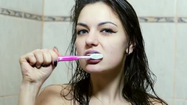 Jeune belle femme se brossant les dents dans la salle de bain vue de face — Video