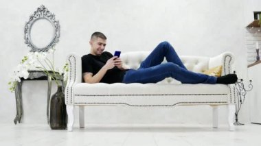 Adam genç kanepede rahatlatıcı ve modern lüks evde smartphone kullanarak arkadaşlarınızla sohbet