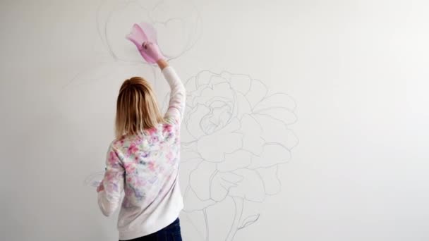 Vrouw graffitikunstenaar schildert pioenrozen bloemen op een witte muur met een borstel — Stockvideo