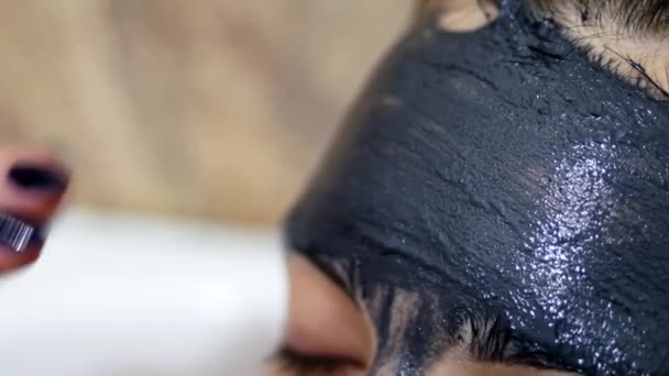 Macro close-up girl puts on the face black cleansing cream mask. Skin care concept — Stock Video