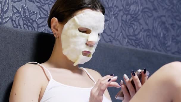 Vrouw met masker op haar gezicht gebruik van mobiele telefoon thuis — Stockvideo