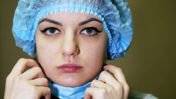 Portret van een vrouwelijke arts, zet op chirurgische masker en camera te kijken — Stockvideo