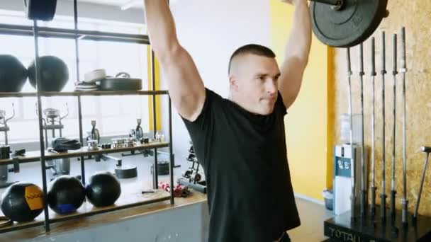 Hombre fuerte haciendo ejercicios de levantamiento de pesas con barra en el gimnasio, levanta la barra sobre la cabeza — Vídeo de stock