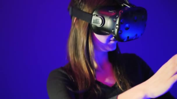 Κοντινό-up γυναίκα πορτραίτο στο ακουστικό VR να διασκεδάσουν και να παίξουν διαδραστικό παιχνίδι βίντεο. Κράνος εικονικής πραγματικότητας σε μπλε φόντο, — Αρχείο Βίντεο