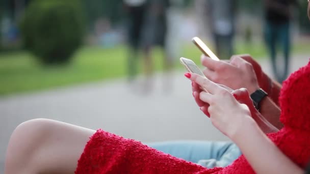 Νέοι άνθρωποι χρησιμοποιεί μια κινητά τηλέφωνα σε εξωτερικούς χώρους. Στο δρόμο, να παρακολουθήσετε φωτογραφίες, χρησιμοποιούν το διαδίκτυο, παίζουν το παιχνίδι, άνθρωποι περνούν από. Κατέχουν το smartphone τους στα χέρια τους. Γκρο πλαν — Αρχείο Βίντεο