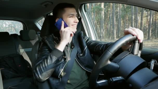 Κομψός άνθρωπος κάθεται στο τιμόνι του αυτοκινήτου και μιλάει στο κινητό τηλέφωνο. Χαμογελαστός τύπος αστειεύεται και χαμόγελο — Αρχείο Βίντεο