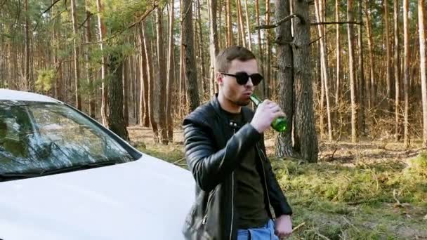 Opilý muž pije pivo u auta a vyhazuje v přírodě láhev. — Stock video