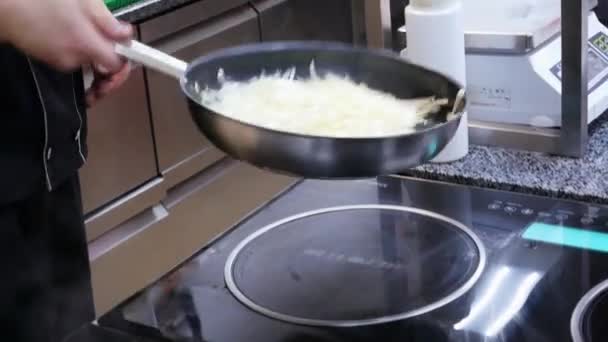 Chef actively working in the kitchen of restaurant mixed onion are roasted in a wok — Stock Video