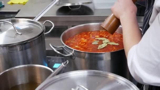 A cook in a restaurant adds spice to the borsch in a large pan — Stock Video