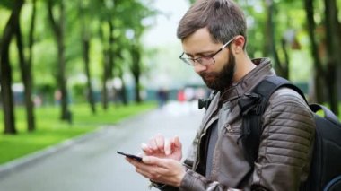 Sakallı adam parkta cep telefonu kullanıyor.