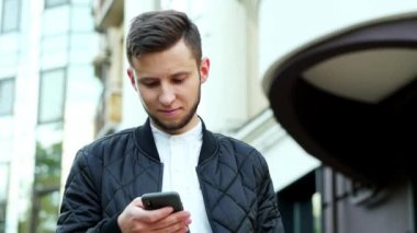 Genç işadamının elinde modern cep telefonu var. Adam SMS yazıyor, sohbet ediyor.