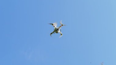 Berrak mavi gökyüzünde uçan küçük quadcopter.