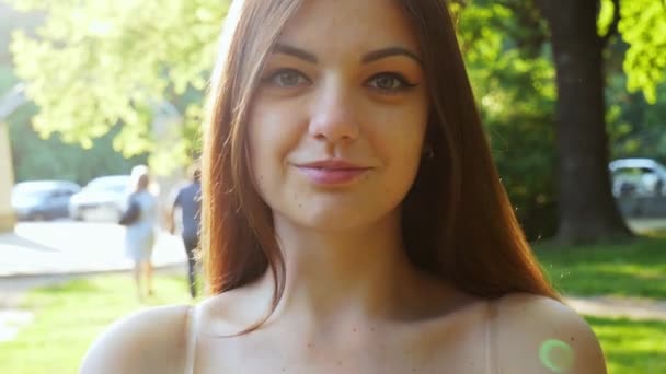 Retrato de una niña en un parque soleado al atardecer, sonriendo — Vídeos de Stock