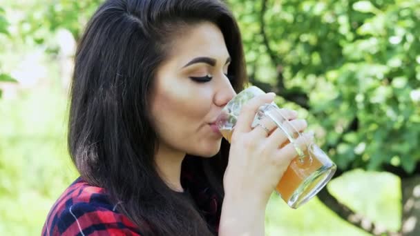 Retrato lateral da jovem mulher bonita feliz que bebe cerveja de vidro, sacia a sede, sorri e olhando para a câmera — Vídeo de Stock