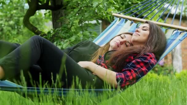 Το λεσβιακό ζευγάρι βρίσκεται στην αιώρα στον κήπο. Δύο λεσβίες γκόμενες αγκαλιάζονται και κοιμούνται — Αρχείο Βίντεο