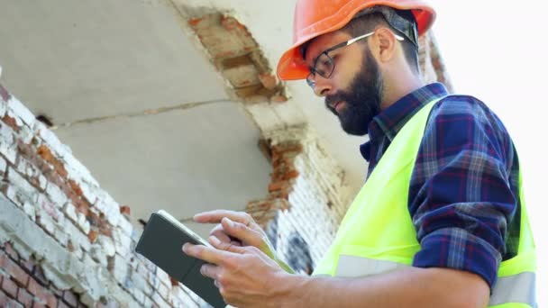 Bir kask bir mühendis Oluşturucu bina yıkım planı hesaplamak ve bir tablet üzerinde inşaat projesine bakıyor — Stok video