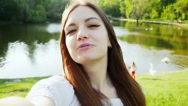ポブショット、ビデオチャット、彼女の友人や家族とのビデオ通話を持つ若い幸せな女性。湖の近くのカメラで手を振って話す観光客 — ストック動画