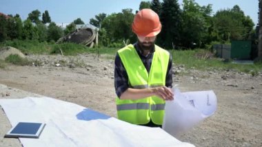 Turuncu kask lı sakallı inşaat mühendisi çizimi analiz ediyor. İnşaata hazırlık