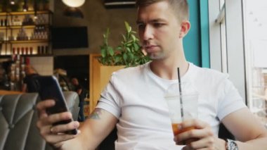 Genç işadamı kafede cep telefonu kullanıyor, soğuk kahve kokteyli içiyor.