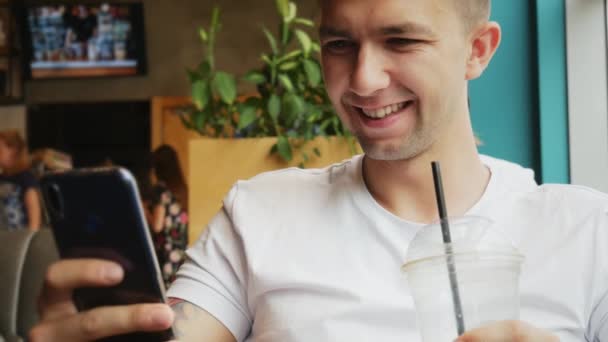 Blízký portrét mladého muže používá mobilní telefon v kavárně, pije studenou kávu koktejl — Stock video