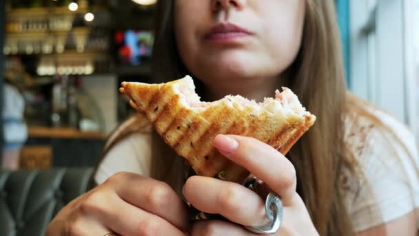 Közeli fel a fiatal éhes nő eszik pirítóst egy kávézóban, gyorsétterem — Stock videók