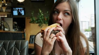 Genç aç kadın bir kafede tost yiyor, fast food restoranında.