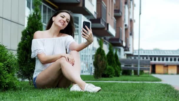 Mooie vrouw praten in video chat via mobiele telefoon, zittend op het gras en spreken met vrienden — Stockvideo