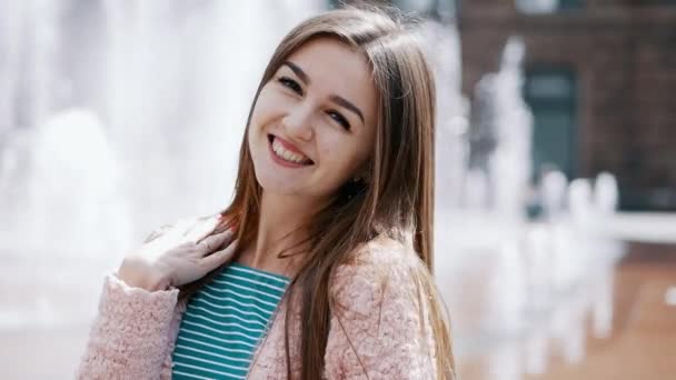 Retrato de estilo de vida de la mujer bastante sonriente en aspecto elegante en la calle de la ciudad, fuente en el fondo — Vídeos de Stock